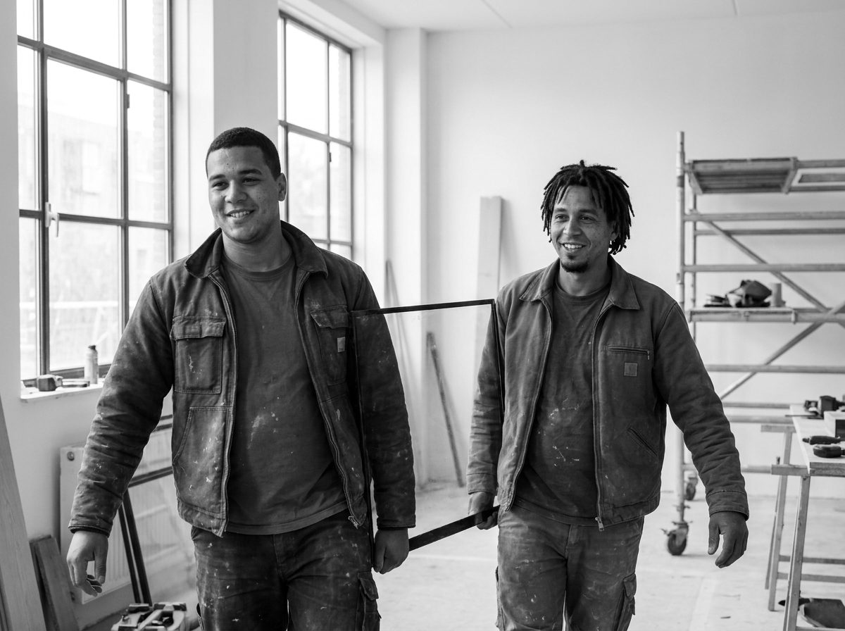 Twee monteurs dragen een grote glaspartij door een pand in aanbouw