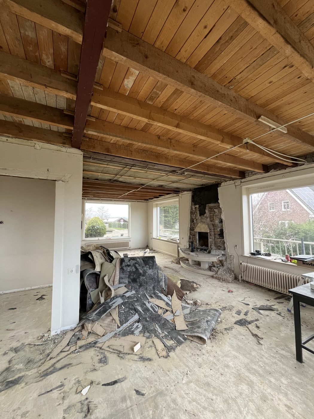 Woonkamer tijdens de sloop, met oud balkenplafond, open haard en een opengebroken vloer
